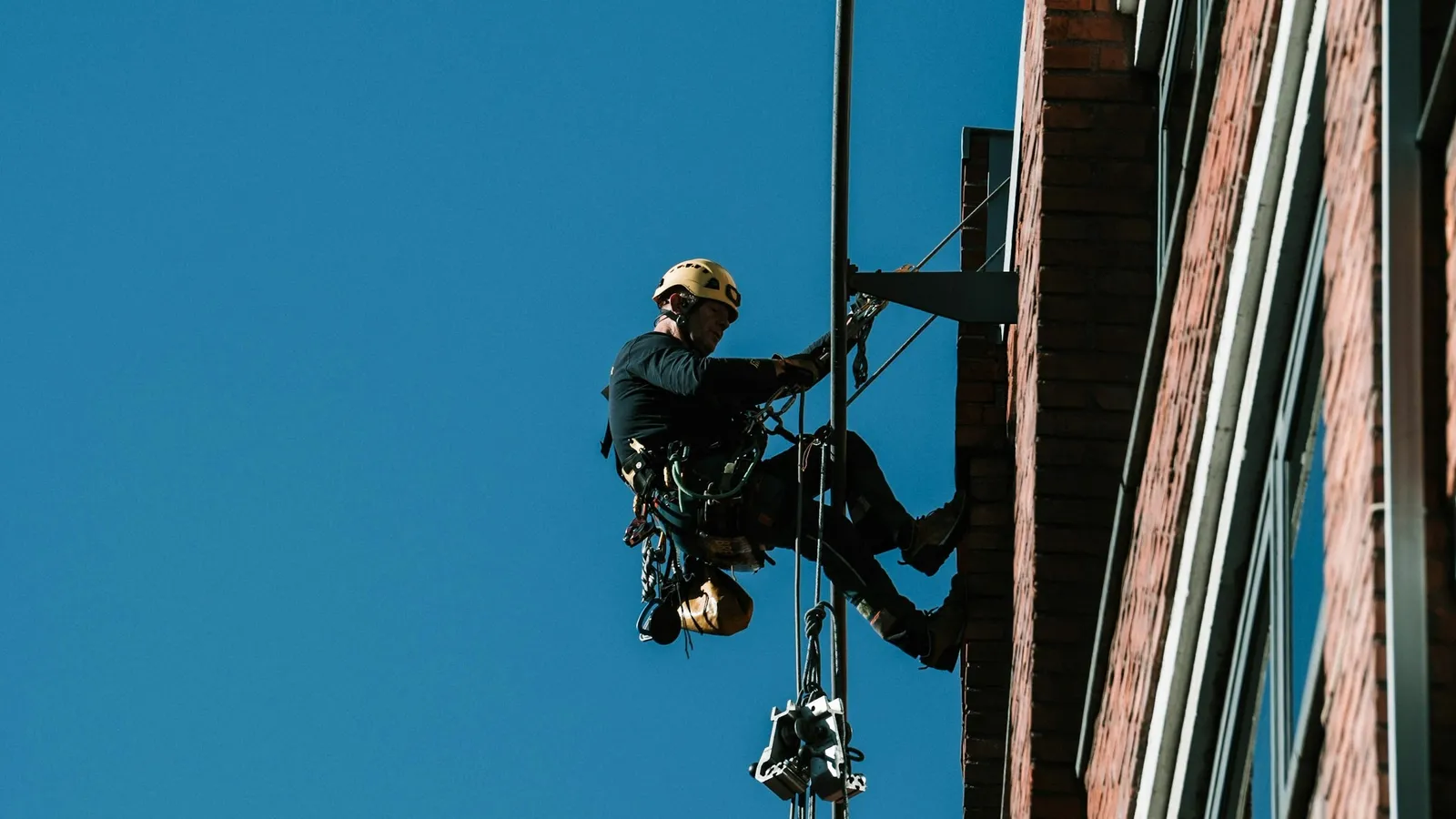 Cordiste suspendu à ses cordes le long d'une façade de briques